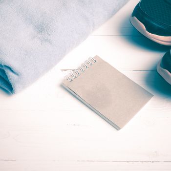 fitness equipment : running shoes,blue towel and notepad on white wood table vintage style