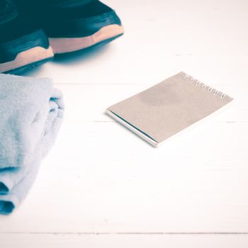 fitness equipment : running shoes,blue towel and notepad on white wood table vintage style