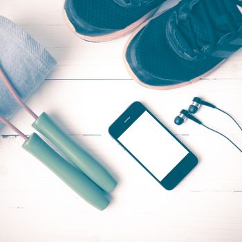 fitness equipment : running shoes,towel,jumping rope and phone on white wood table vintage style