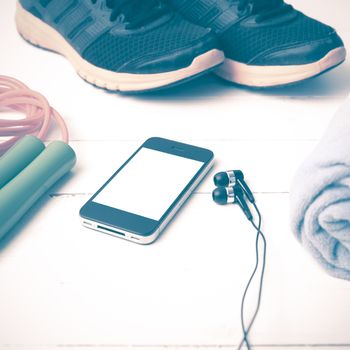 fitness equipment : running shoes,towel,jumping rope and phone on white wood table vintage style