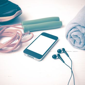 fitness equipment : running shoes,towel,jumping rope and phone on white wood table vintage style