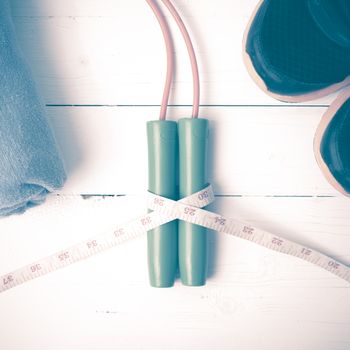 fitness equipment : running shoes,towel,jumping rope and measuring tape on white wood table vintage style
