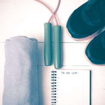 fitness equipment : running shoes,towel,jumping rope and notebook write to do list on white wood table vintage style