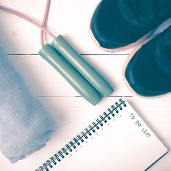 fitness equipment : running shoes,towel,jumping rope and notebook write to do list on white wood table vintage style