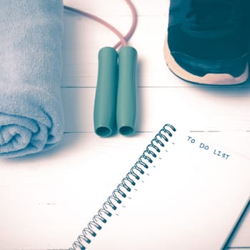 fitness equipment : running shoes,towel,jumping rope and notebook write to do list on white wood table vintage style