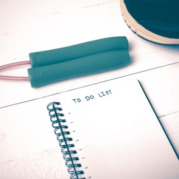 fitness equipment : running shoes,jumping rope and notebook write to do list on white wood table vintage style