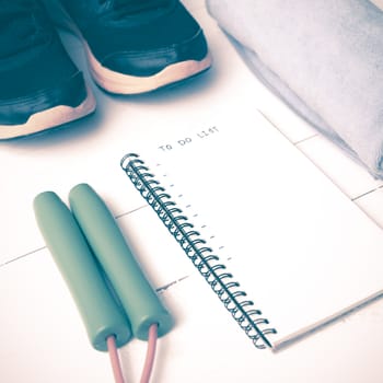 fitness equipment : running shoes,towel,jumping rope and notebook write to do list on white wood table vintage style