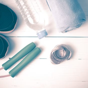 fitness equipment : running shoes,towel,jumping rope,water bottle and measuring tape on white wood table vintage style