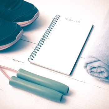 fitness equipment : running shoes,towel,jumping rope and notebook write to do list on white wood table vintage style
