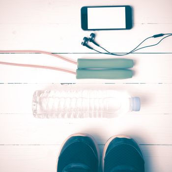 fitness equipment : running shoes,jumping rope,water bottle and phone on white wood table vintage style