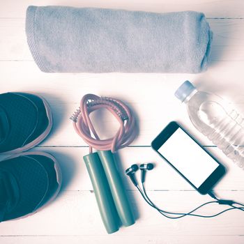 fitness equipment : running shoes,towel,jumping rope,water bottle and phone on white wood table vintage style