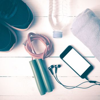 fitness equipment : running shoes,towel,jumping rope,water bottle and phone on white wood table vintage style