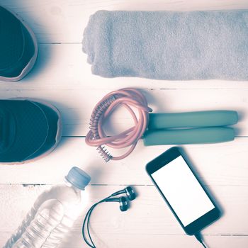 fitness equipment : running shoes,towel,jumping rope,water bottle and phone on white wood table vintage style