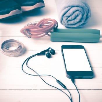 fitness equipment : running shoes,towel,jumping rope,phone and measuring tape on white wood table vintage style