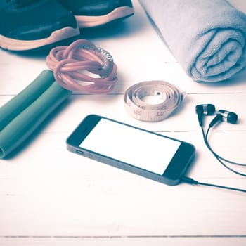 fitness equipment : running shoes,towel,jumping rope,water bottle,phone and measuring tape on white wood table vintage style