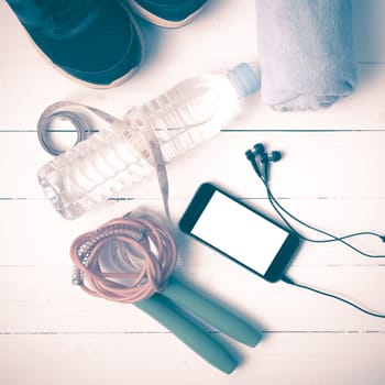 fitness equipment : running shoes,towel,jumping rope,water bottle,phone and measuring tape on white wood table vintage style