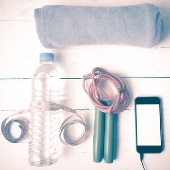 fitness equipment :towel,jumping rope,water bottle,phone and measuring tape on white wood table vintage style