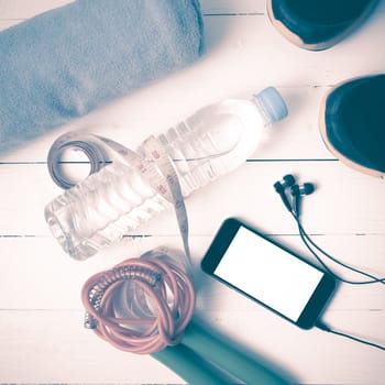 fitness equipment : running shoes,towel,jumping rope,water bottle,phone and measuring tape on white wood table vintage style