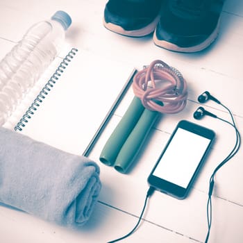 fitness equipment : running shoes,towel,jumping rope,water bottle,phone and notepad on white wood table vintage style