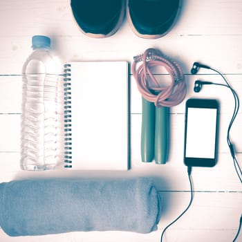 fitness equipment : running shoes,towel,jumping rope,water bottle,phone and notepad on white wood table vintage style