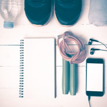 fitness equipment : running shoes,towel,jumping rope,water bottle,phone and notepad on white wood table vintage style