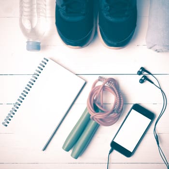 fitness equipment : running shoes,towel,jumping rope,water bottle,phone and notepad on white wood table vintage style