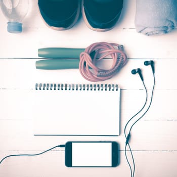 fitness equipment : running shoes,towel,jumping rope,water bottle,phone and notepad on white wood table vintage style