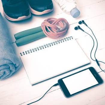 fitness equipment : running shoes,towel,jumping rope,water bottle,phone and notepad on white wood table vintage style