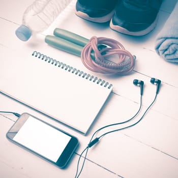 fitness equipment : running shoes,towel,jumping rope,water bottle,phone and notepad on white wood table vintage style