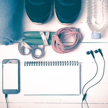 fitness equipment : running shoes,towel,jumping rope,water bottle,phone,notepad and measuring tape on white wood table vintage style