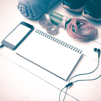 fitness equipment : running shoes,towel,jumping rope,phone,notepad and measuring tape on white wood table vintage style