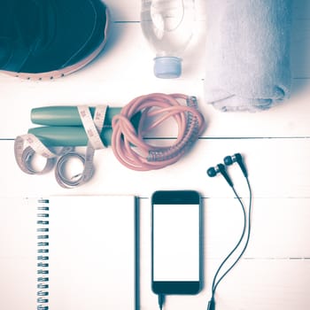 fitness equipment : running shoes,towel,jumping rope,water bottle,phone,notepad and measuring tape on white wood table vintage style