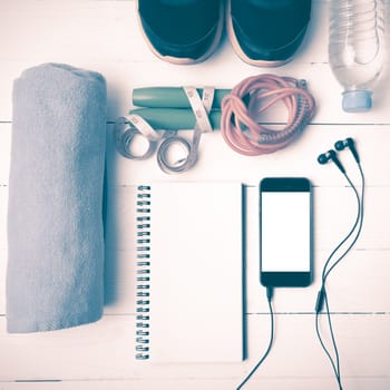 fitness equipment : running shoes,towel,jumping rope,water bottle,phone,notepad and measuring tape on white wood table vintage style