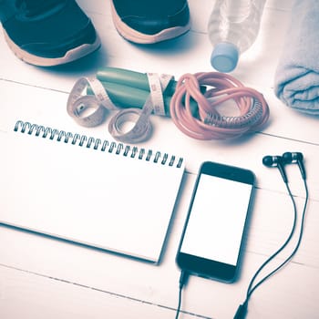 fitness equipment : running shoes,towel,jumping rope,water bottle,phone,notepad and measuring tape on white wood table vintage style