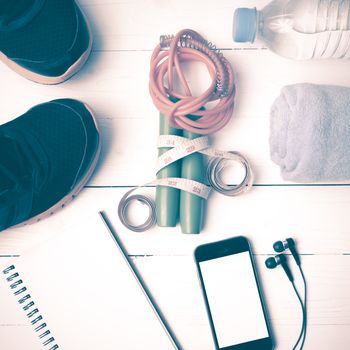 fitness equipment : running shoes,towel,jumping rope,water bottle,phone,notepad and measuring tape on white wood table vintage style