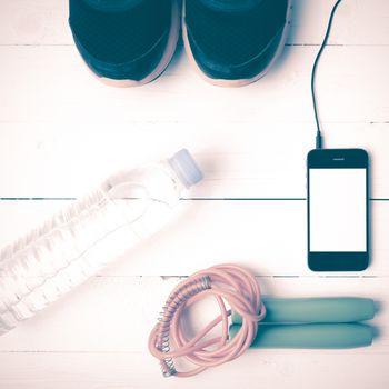 fitness equipment : running shoes,jumping rope,phone and water bottle on white wood table vintage style