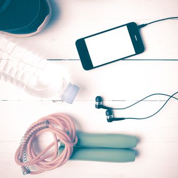 fitness equipment : running shoes,jumping rope,phone and water bottle on white wood table vintage style