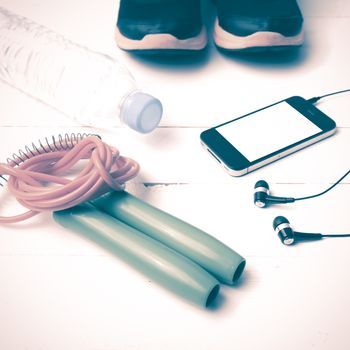 fitness equipment : running shoes,jumping rope,phone and water bottle on white wood table vintage style