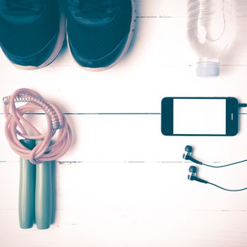 fitness equipment : running shoes,jumping rope,phone and water bottle on white wood table vintage style