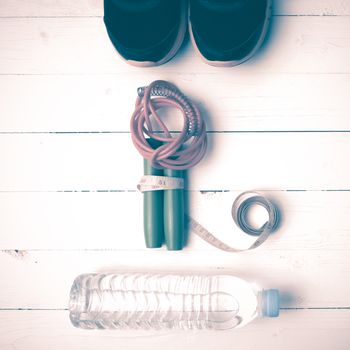 fitness equipment : running shoes,jumping rope,measuring tape and water bottle on white wood table vintage style