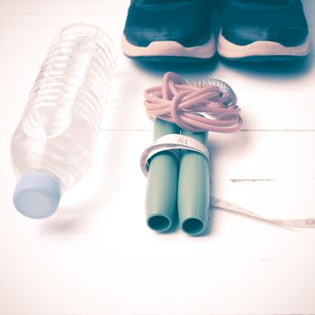 fitness equipment : running shoes,jumping rope,measuring tape and water bottle on white wood table vintage style