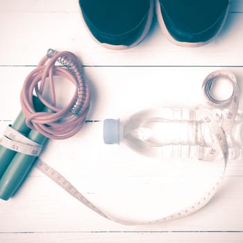 fitness equipment : running shoes,jumping rope,measuring tape and water bottle on white wood table vintage style