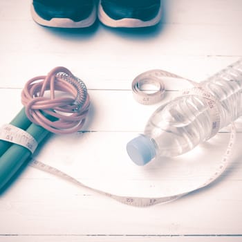 fitness equipment : running shoes,jumping rope,measuring tape and water bottle on white wood table vintage style