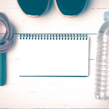 fitness equipment : running shoes,jumping rope,drinking water and notepad on white wood table vintage style