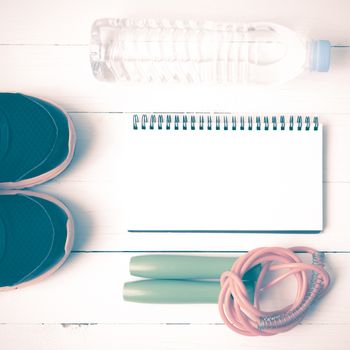 fitness equipment : running shoes,jumping rope,drinking water and notepad on white wood table vintage style