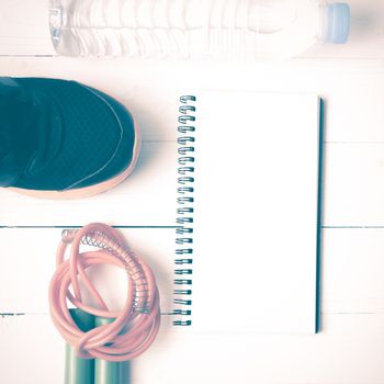 fitness equipment : running shoes,jumping rope,drinking water and notepad on white wood table vintage style