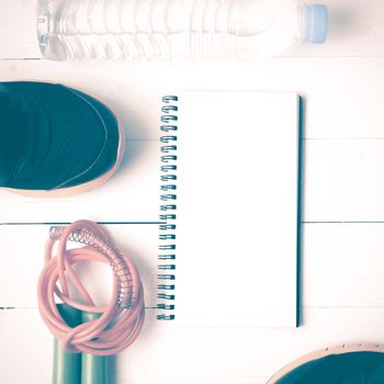 fitness equipment : running shoes,jumping rope,drinking water and notepad on white wood table vintage style