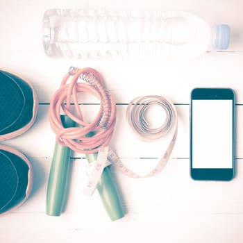 fitness equipment : running shoes,jumping rope,drinking water,measuring tape and phone on white wood table vintage style