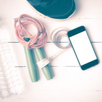 fitness equipment : running shoes,jumping rope,drinking water,measuring tape and phone on white wood table vintage style