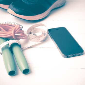 fitness equipment : running shoes,jumping rope,measuring tape and phone on white wood table vintage style